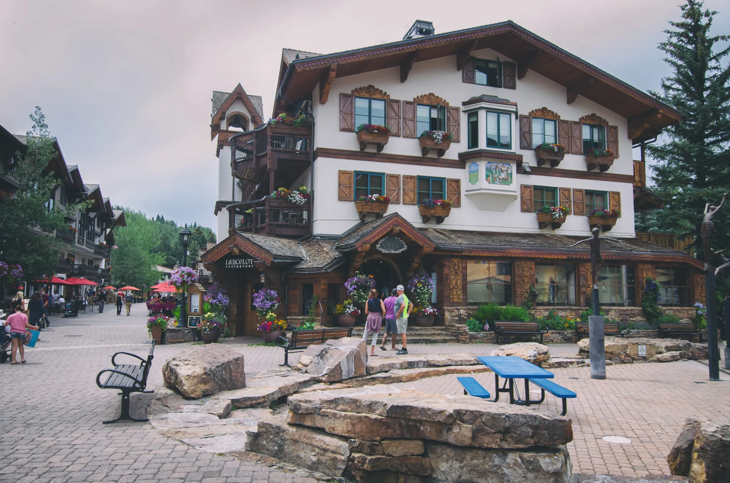 An alpine-style chalet with flower-box windows and the Lancelot restaurant sign above a cobblestone plaza in Vail, Colorado.