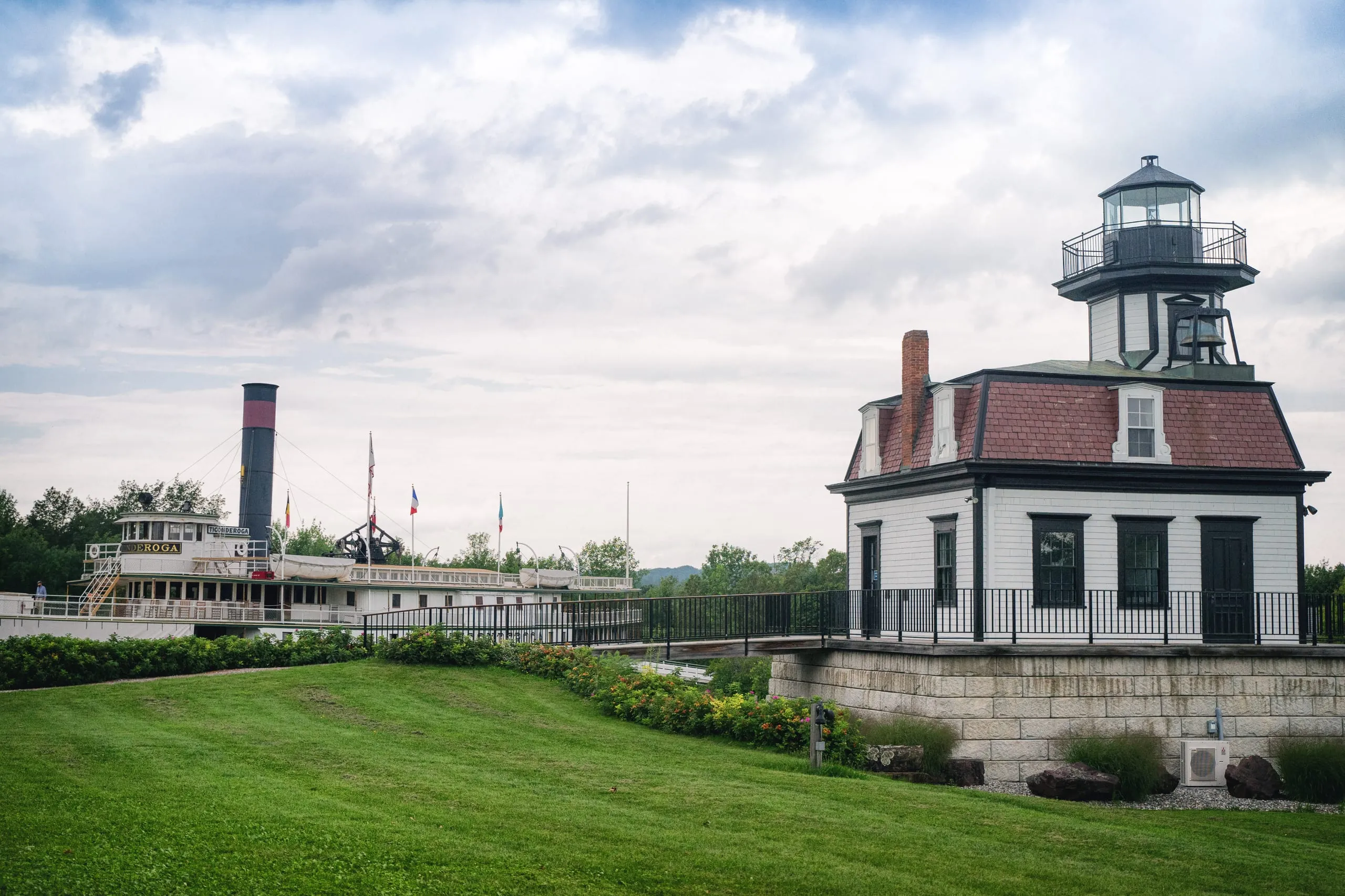 A lighthouse and the steamboat Ticonderoga sit on a manicured lawn at a Vermont museum.