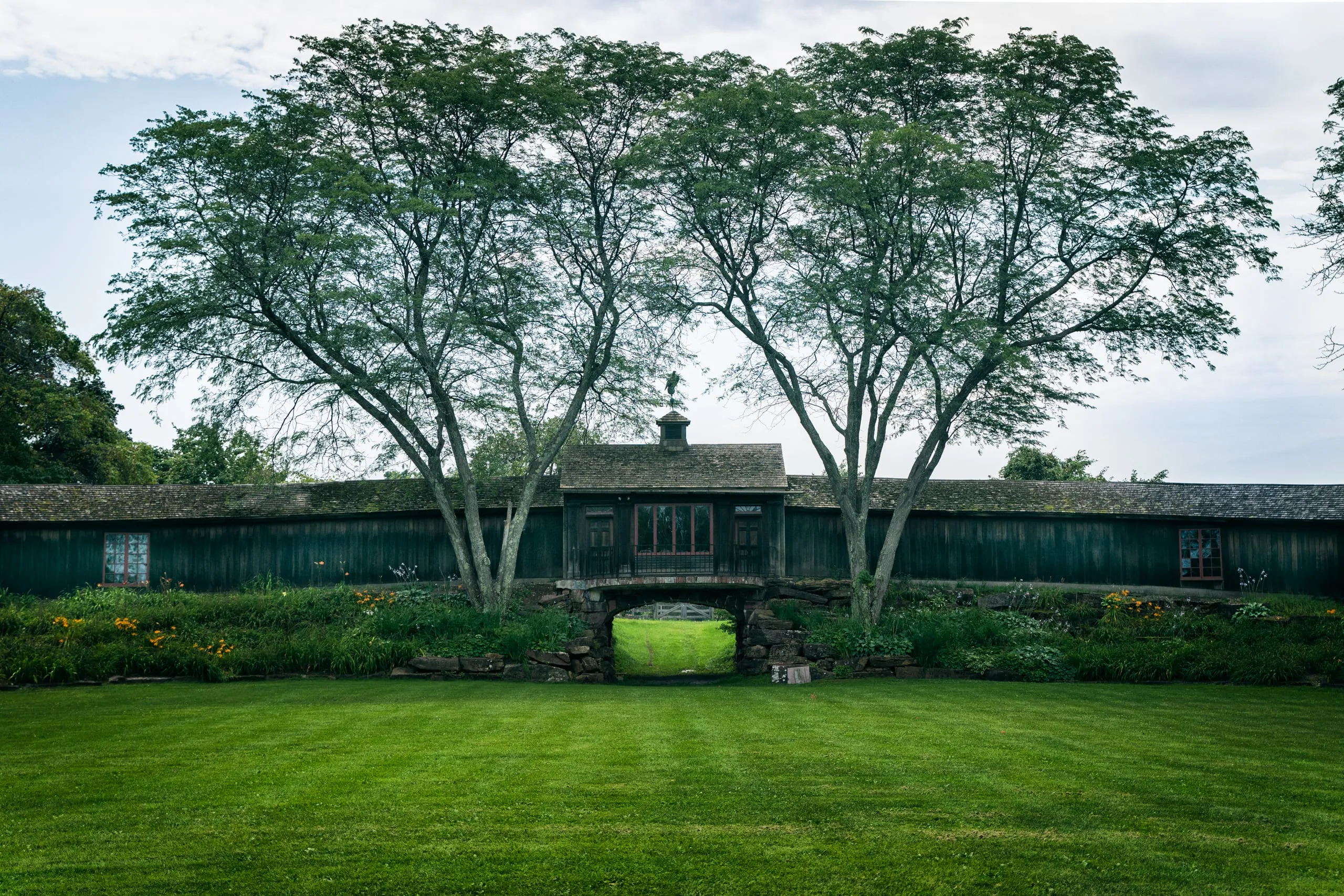Dark carriage barn flanked by two trees above a green lawn at Shelburne, Vermont