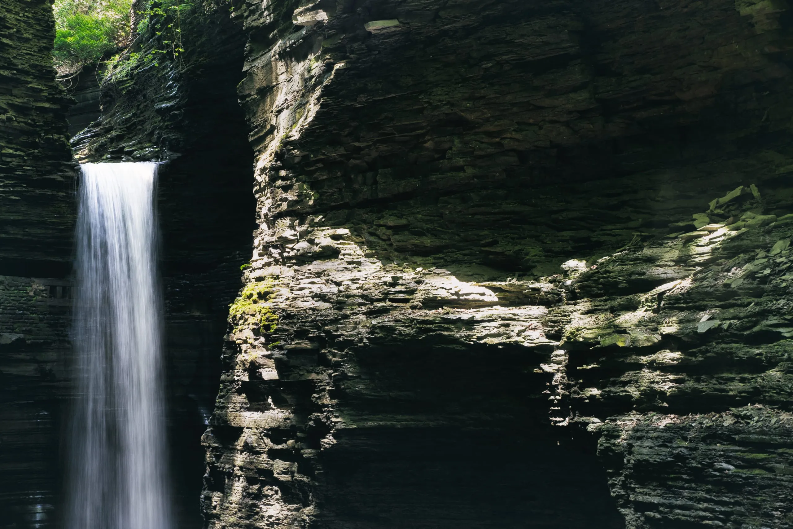 Cavern Cascade waterfall plunging past layered shale walls in Watkins Glen gorge