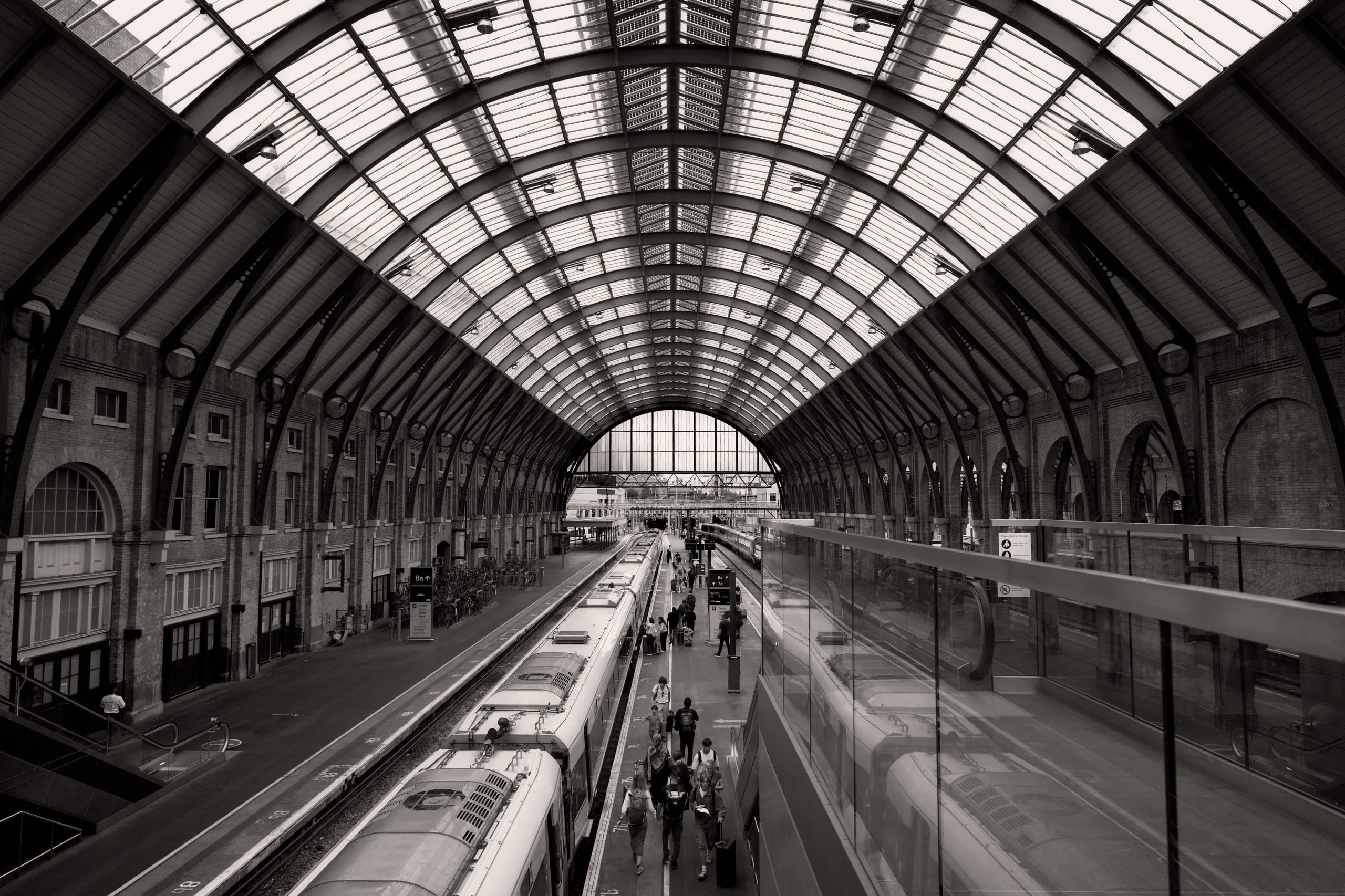 Black and white photograph of the arched train shed at King's Cross station in London, with passengers walking along a platform beside a waiting train.