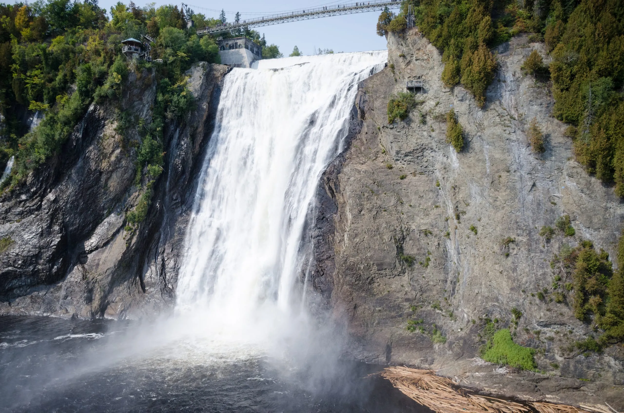 A tall waterfall plunging down a sheer cliff beneath a suspension footbridge near Quebec City, Canada.