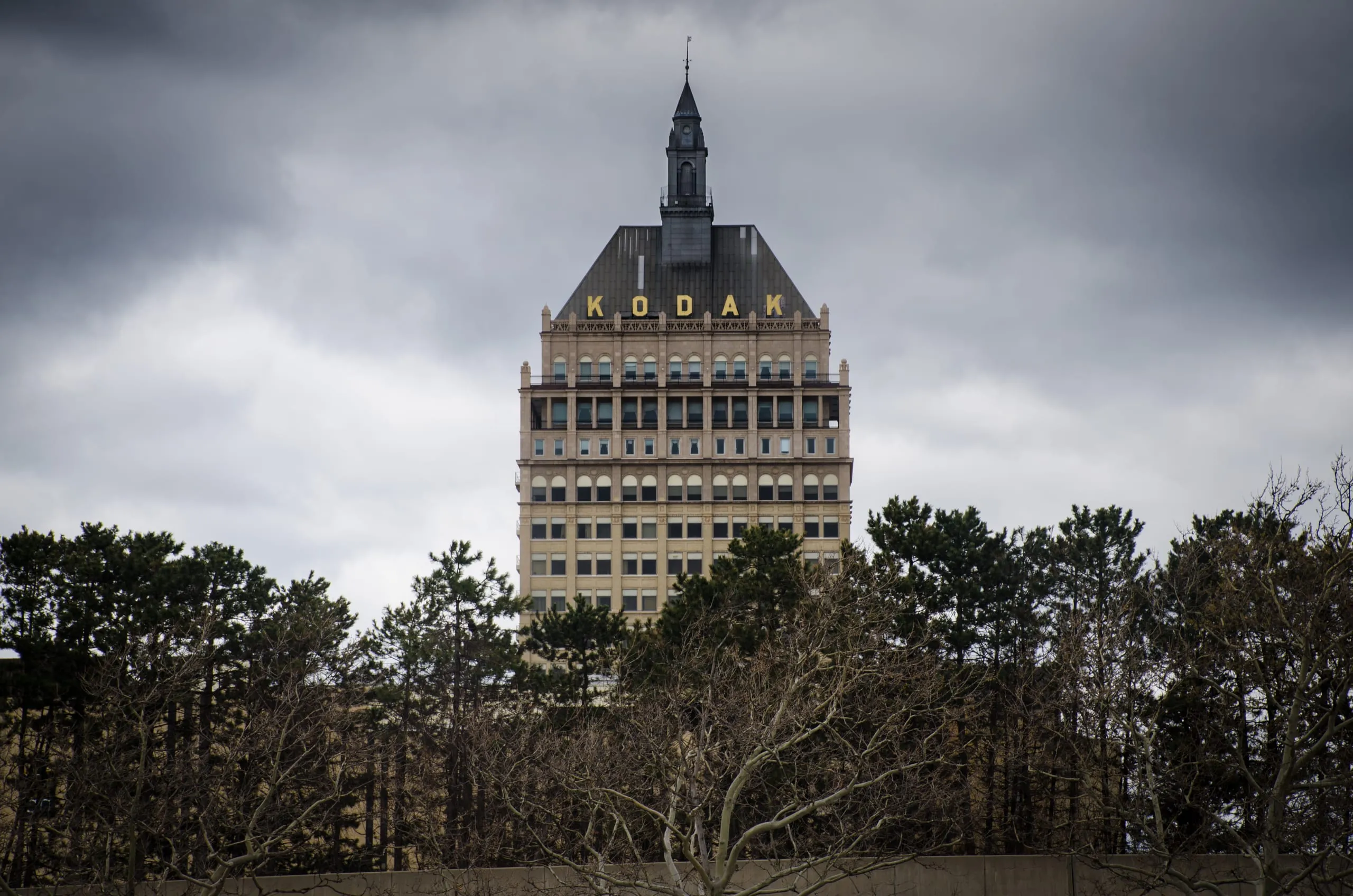 The Kodak Tower rises above bare trees under a heavy gray sky in Rochester, NY.