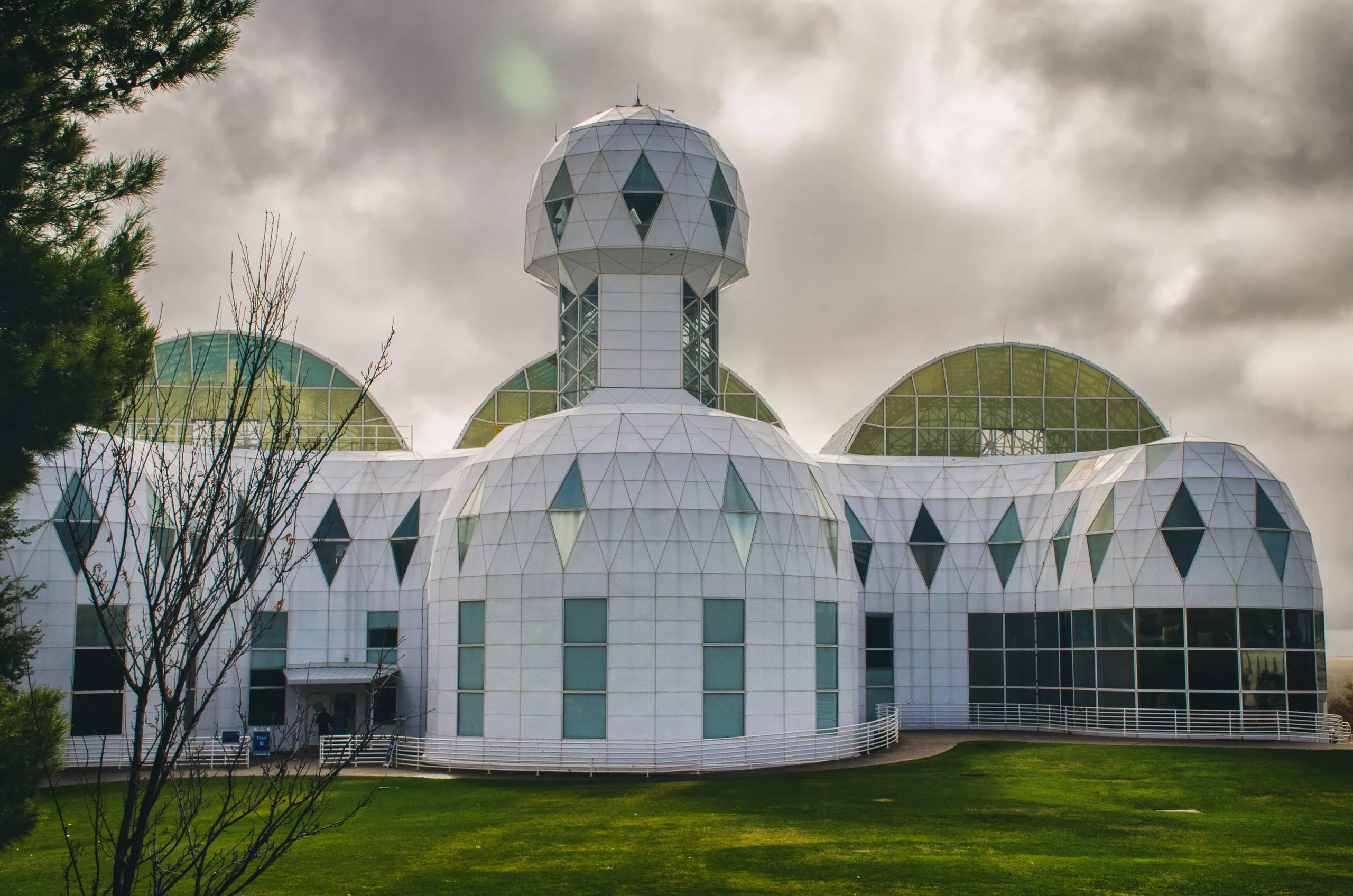 The white geodesic domes and sphered tower of a research campus sit on a green lawn under gray Arizona clouds.