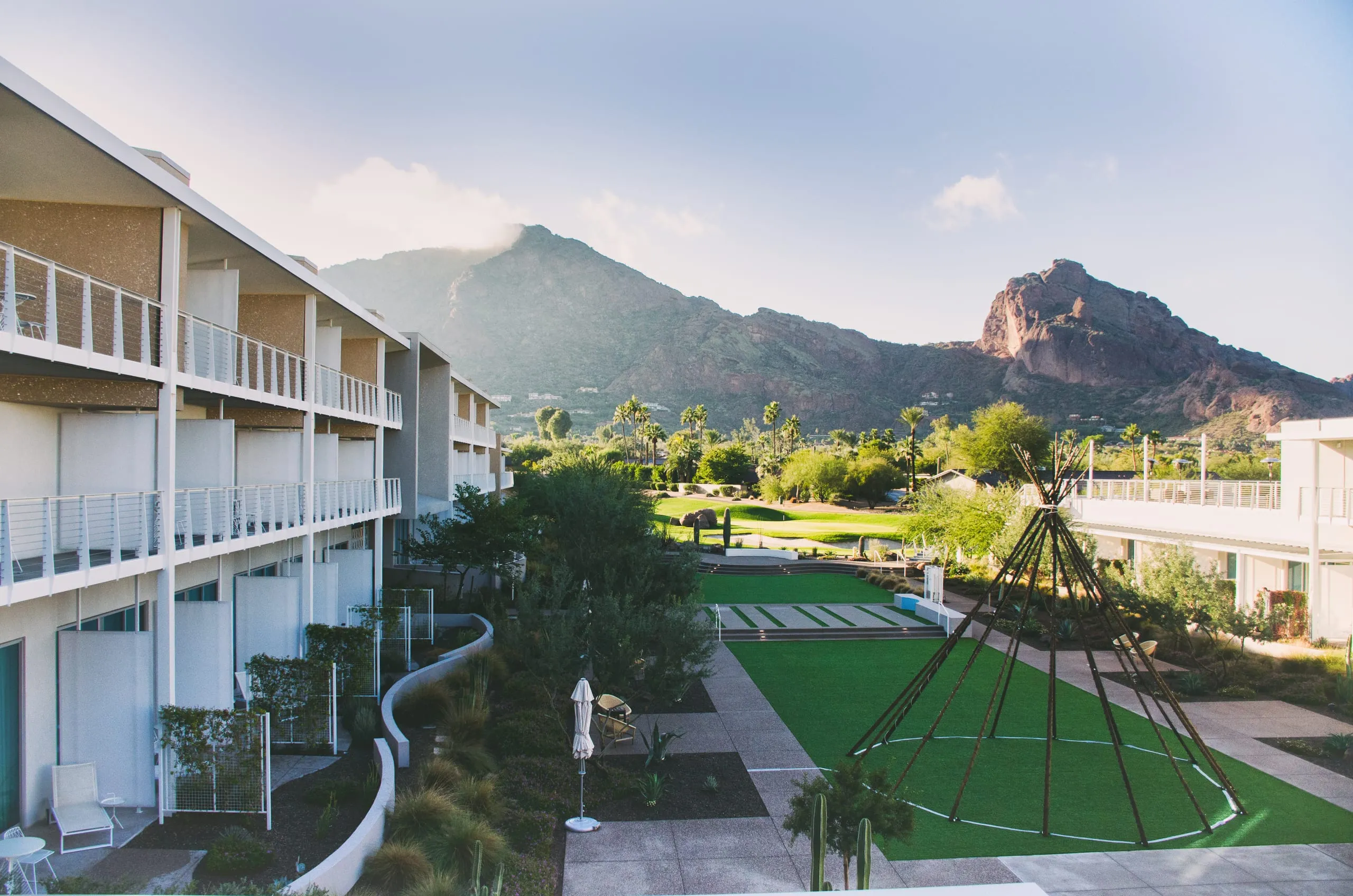 A modern resort courtyard with a bare teepee frame and green lawn faces Camelback Mountain in Arizona.