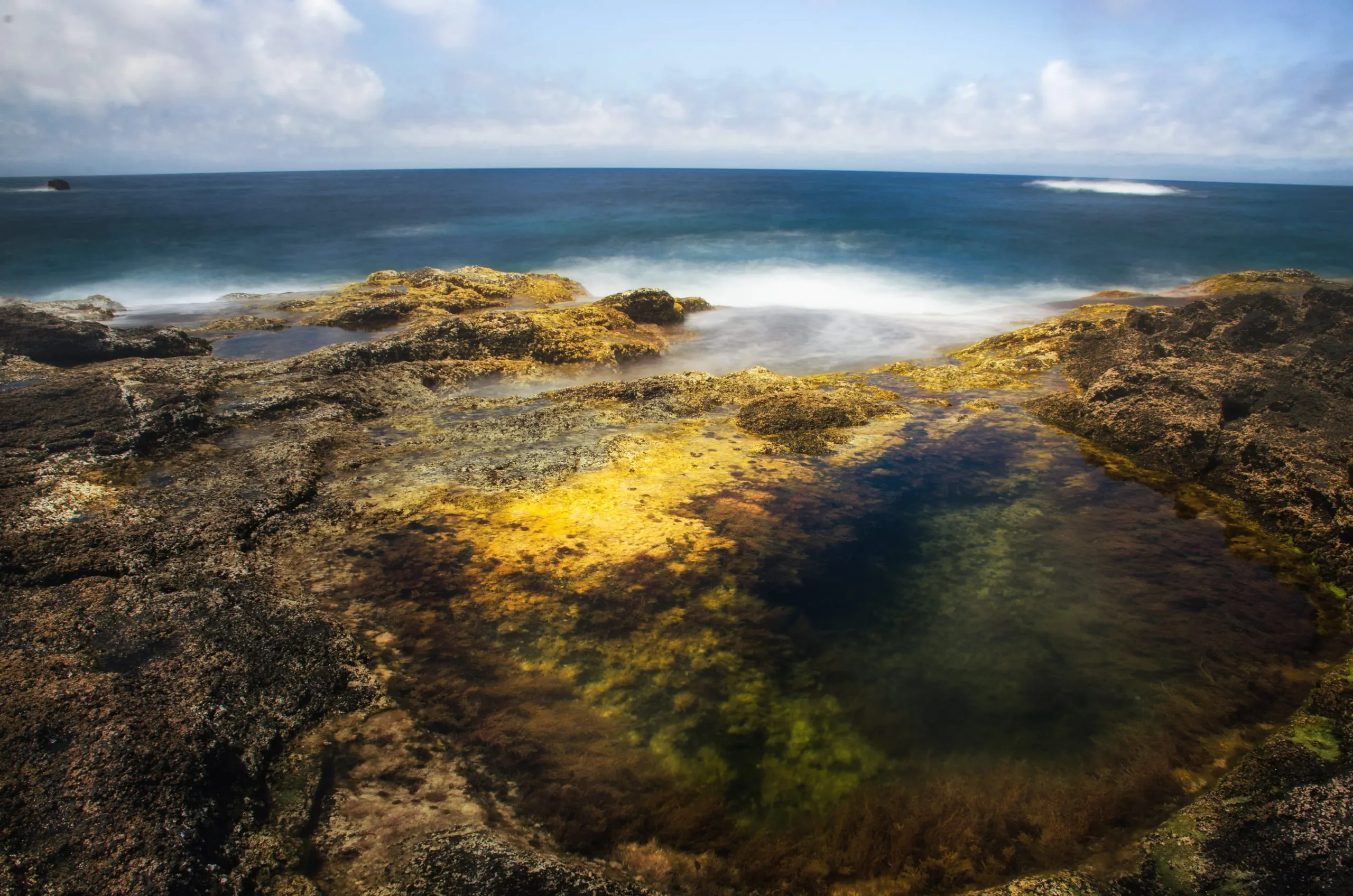 Long-exposure surf washing gold light through volcanic tidepools in the Azores