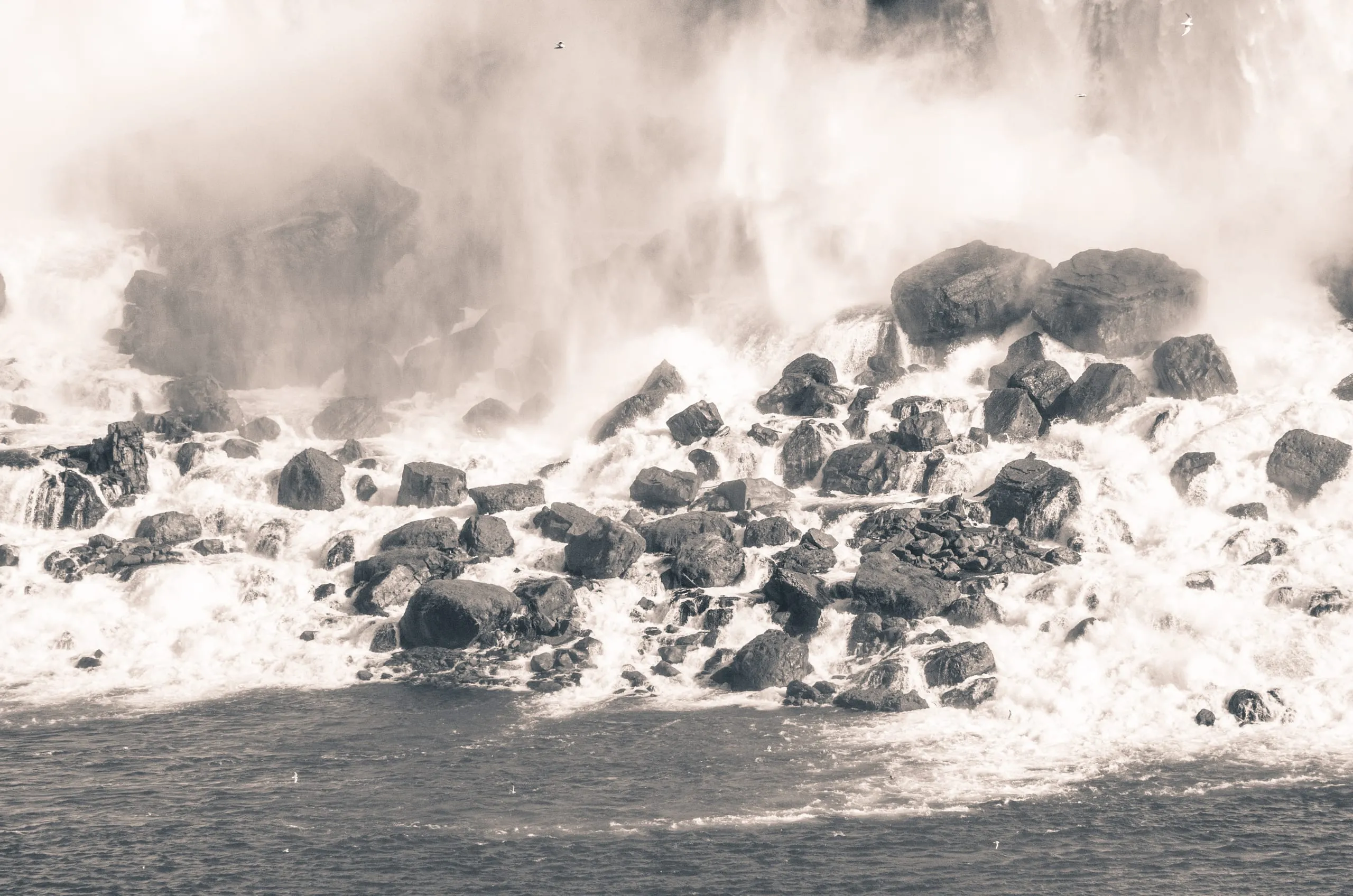 Black and white photograph of whitewater exploding over rocks at the base of Niagara Falls