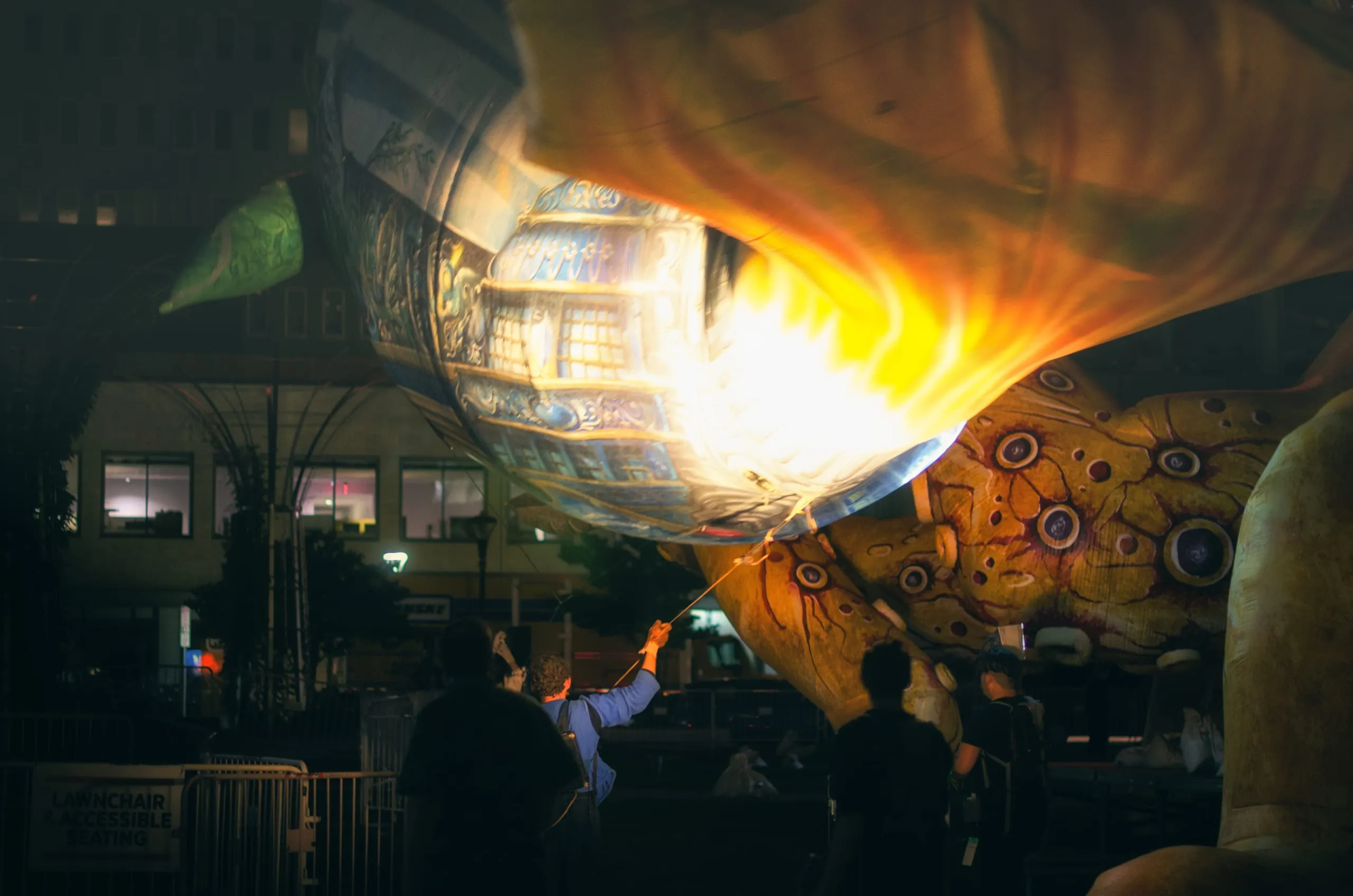 People raising and lighting a large illuminated lantern glowing orange at a night festival, Rochester
