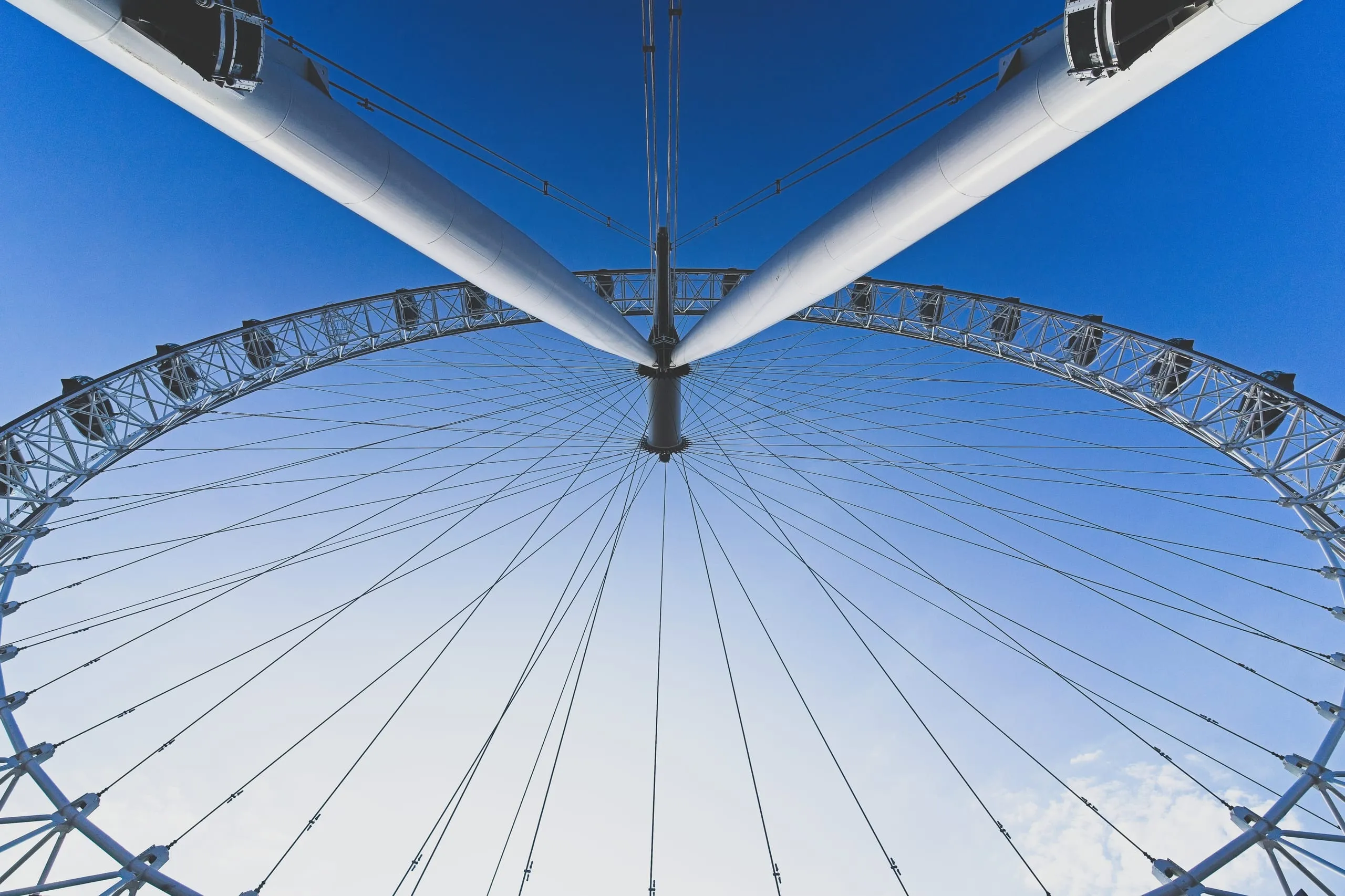 Photograph looking straight up through the spinning spokes and cables of the London Eye against a clear blue sky in London, England.