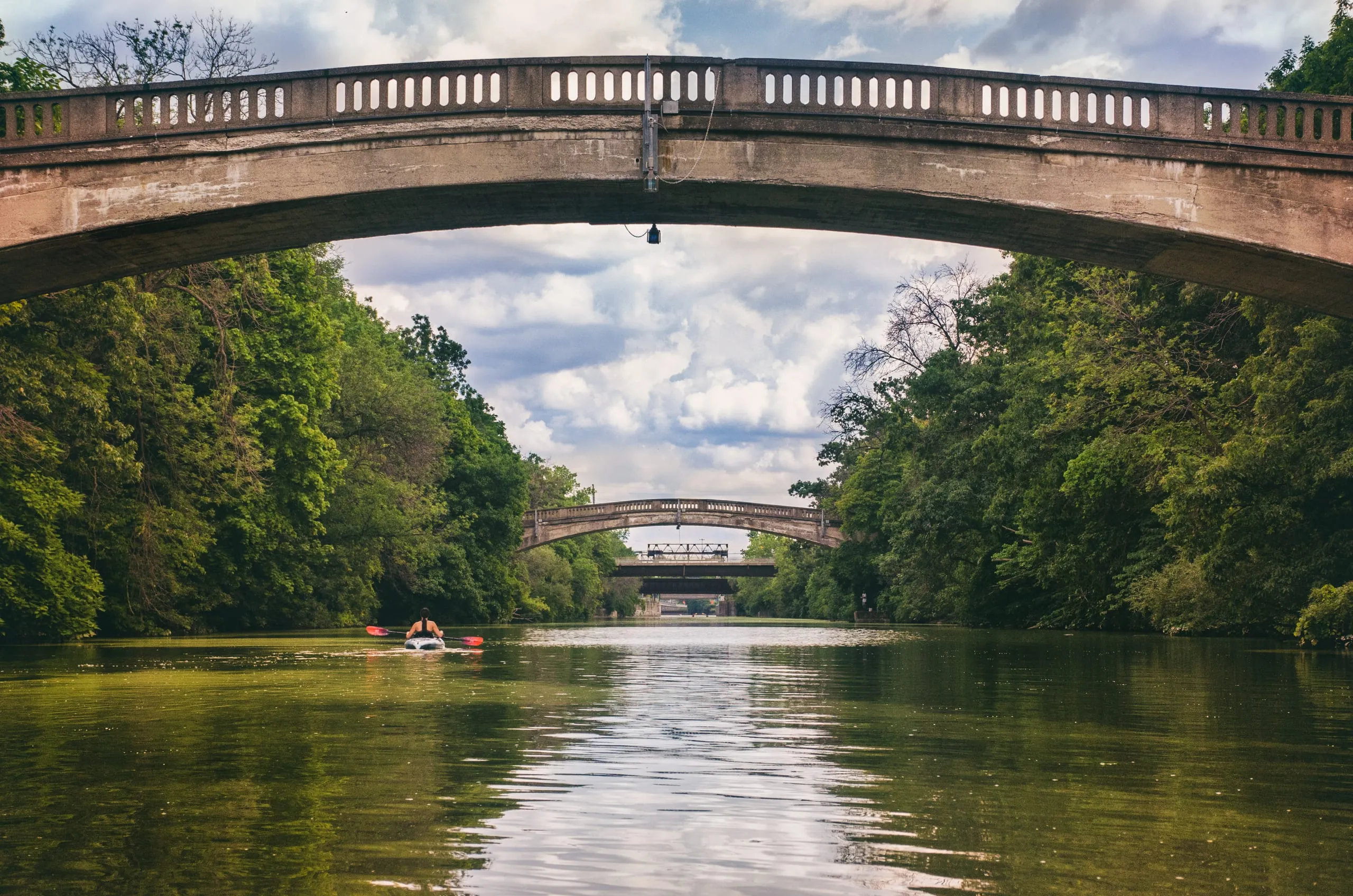 Kayaker paddling the Erie Canal beneath a series of stone arch bridges near Rochester, New York