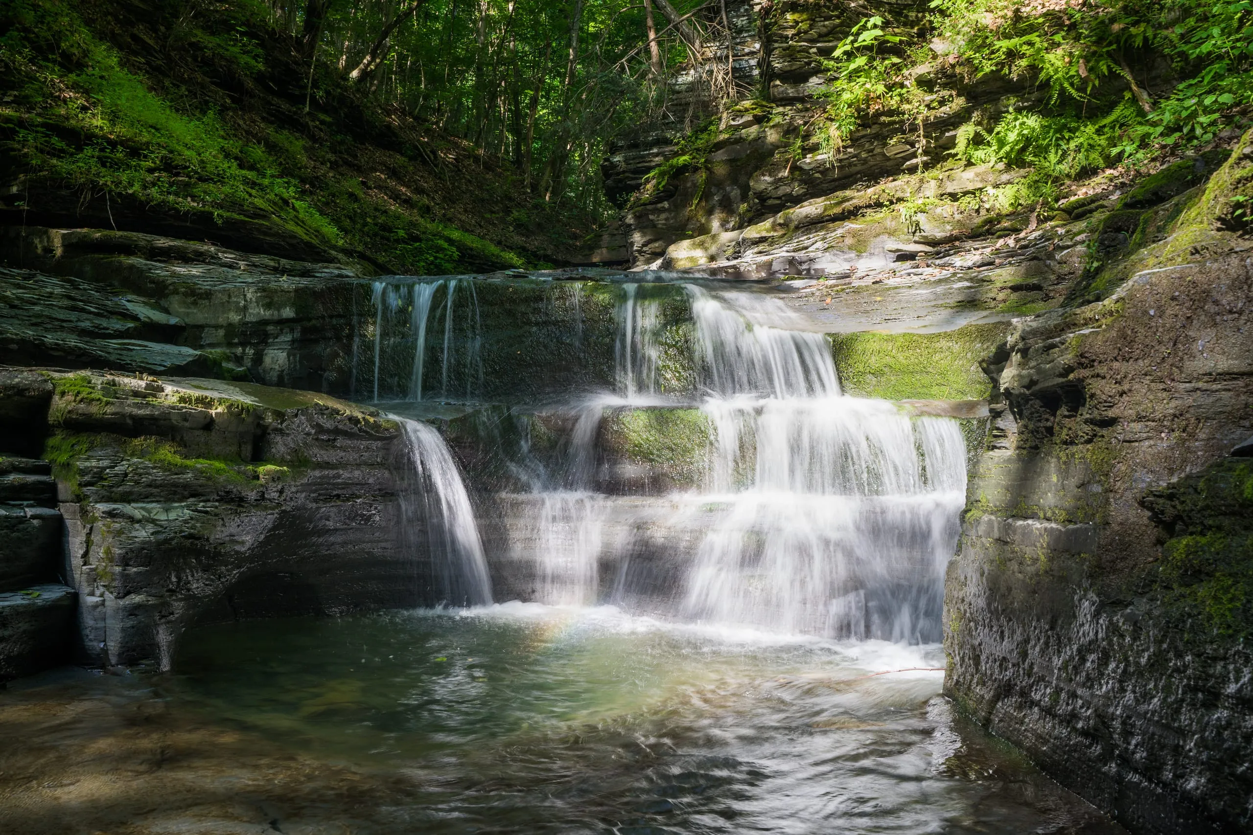 Tiered cascades stepping down into a green plunge pool in Watkins Glen gorge