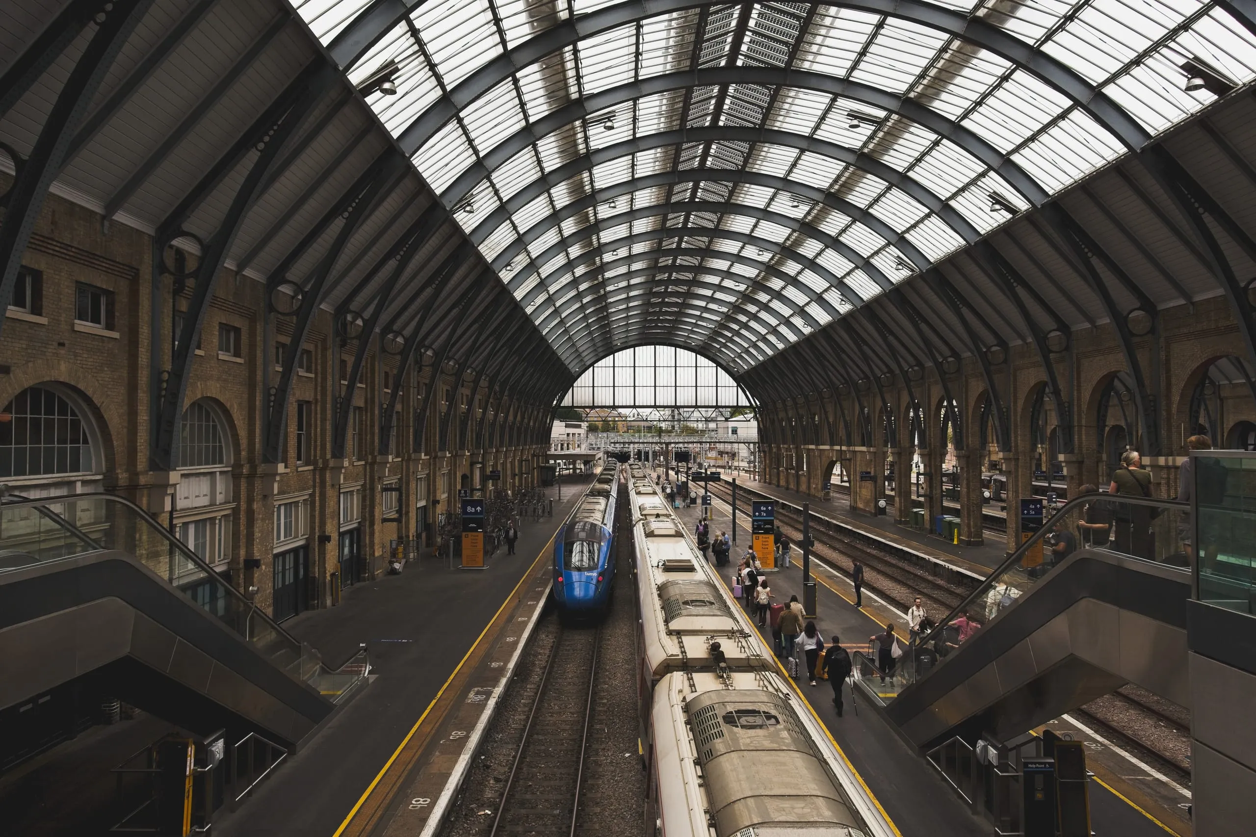 A photograph looking down the platforms of King's Cross station in London beneath its arched Victorian train shed, with a blue train and waiting passengers.