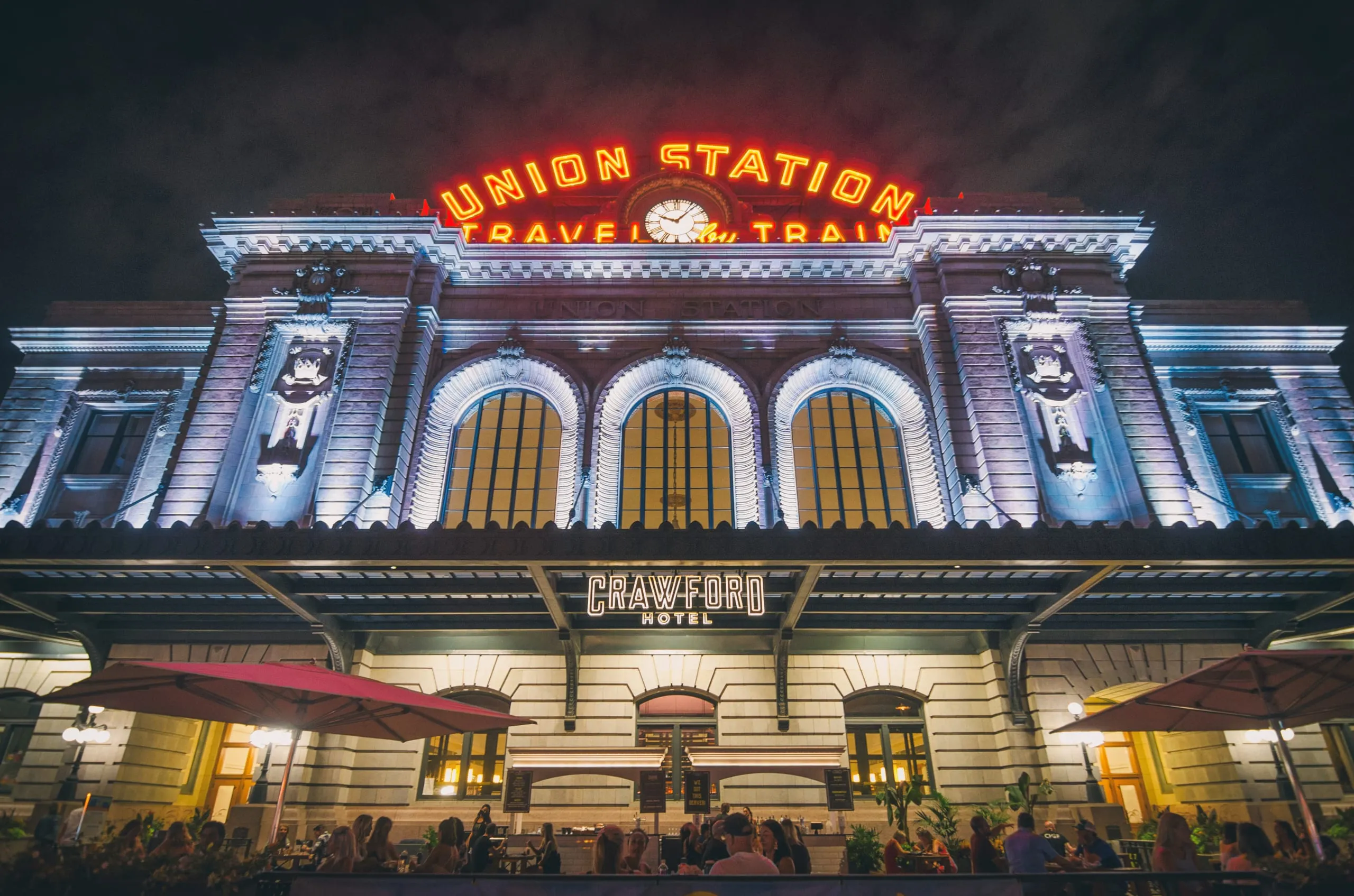 Union Station's neon 'Travel by Train' sign glowing at night in Denver