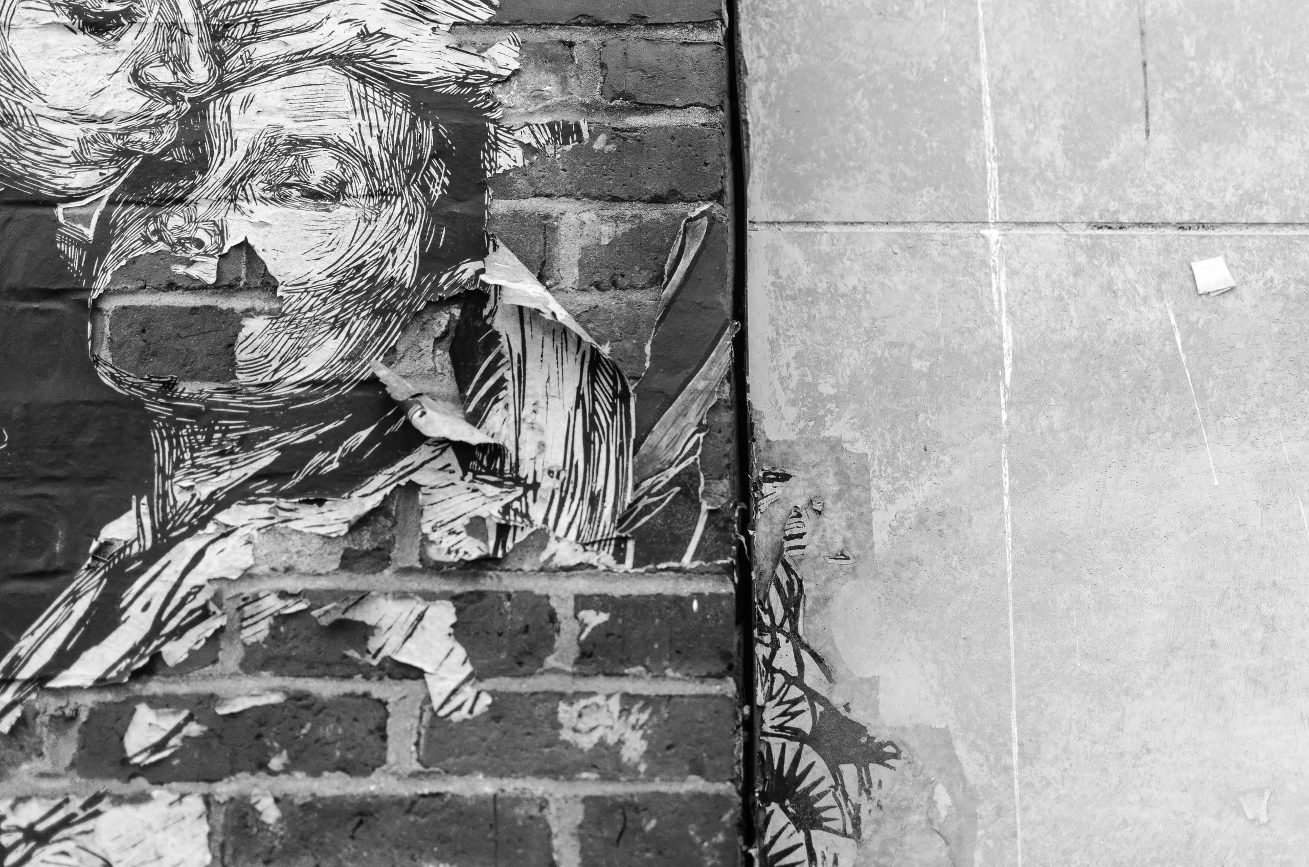 Black and white wheat-paste portrait peeling from a brick wall in Portland, Maine